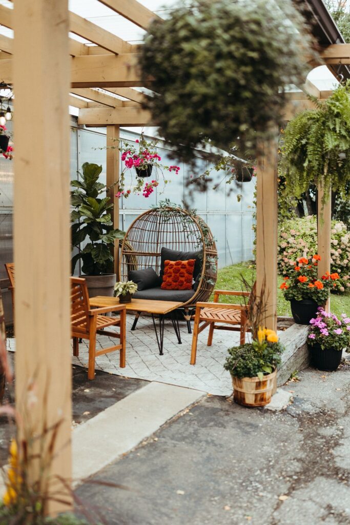 The outdoor gardens with a tall wooden trellis, hanging plants, and modern woven chairs at The Greenhouse At Bittersweet.