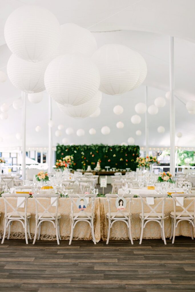 A reception set under a white tent and decorated with white balloons and string lights.